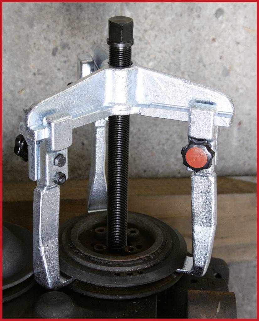 Ein Schraubabzieher fixiert ein Metallwerkstück auf einer Werkbank. Werkzeug zeigt robuste Metallkonstruktion.