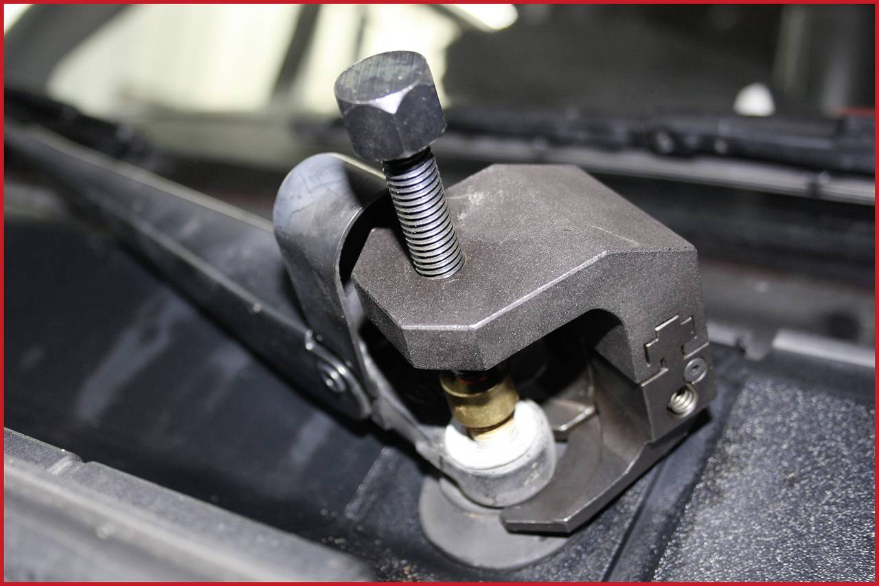 Nahaufnahme eines Kfz-Werkzeugs, das einen Scheibenwischerarm von einem Auto entfernt. Das Werkzeug ist auf dem Gelenk montiert.