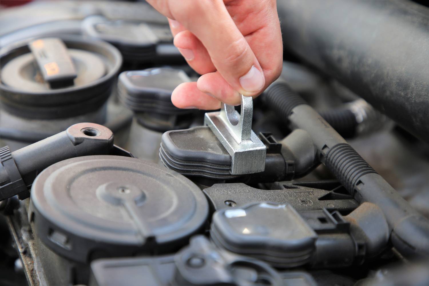 Eine Hand platziert ein Metallteil auf einem Motor. Der Fokus liegt auf der Installation oder dem Austausch von Autoteilen.