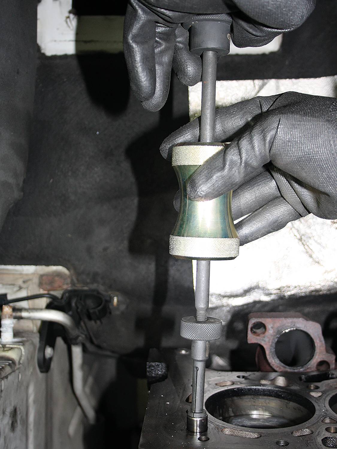 Mechaniker in schwarzen Handschuhen verwendet Spezialwerkzeug zur Installation eines Ventils im Motorblock.