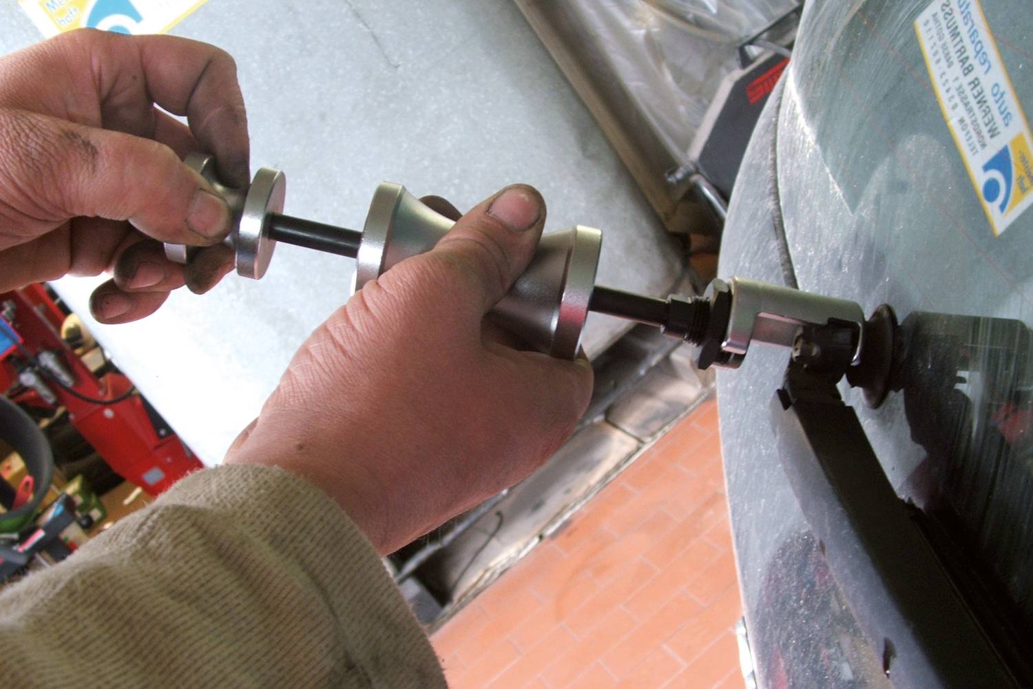 Eine Person repariert oder montiert eine Autoteil mit Werkzeug, im Fokus ist ein Metallstab, der an einem Fahrzeug verwendet wird.