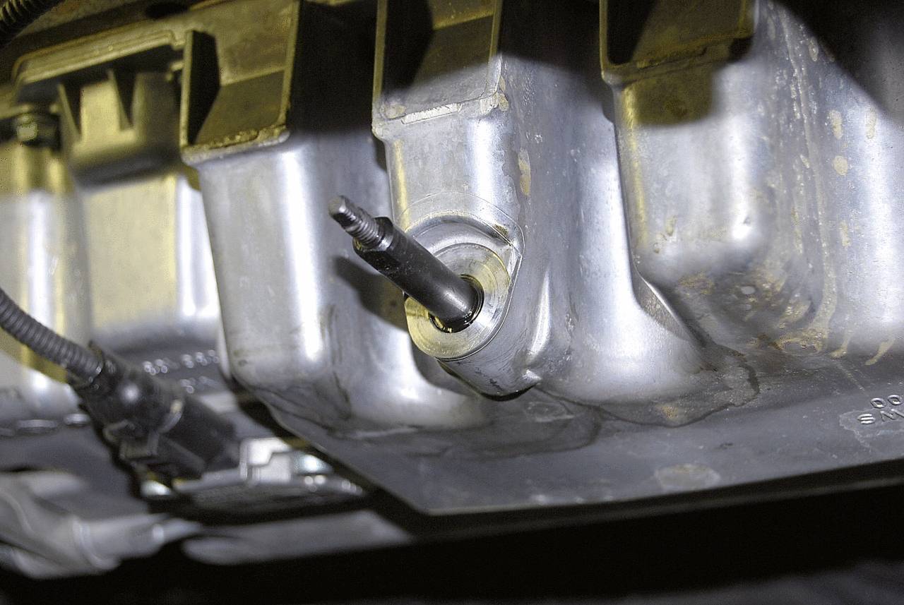 Ölablassschraube an einem Motorblock, teilweise geöffnet, mit sichtbarem Ölfluss. Wichtig für Wartungsaufgaben am Fahrzeug.