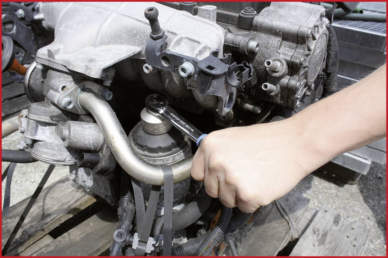 Eine Person repariert einen Motor, indem sie mit einem Schraubenschlüssel an einer Schlauchverbindung arbeitet.