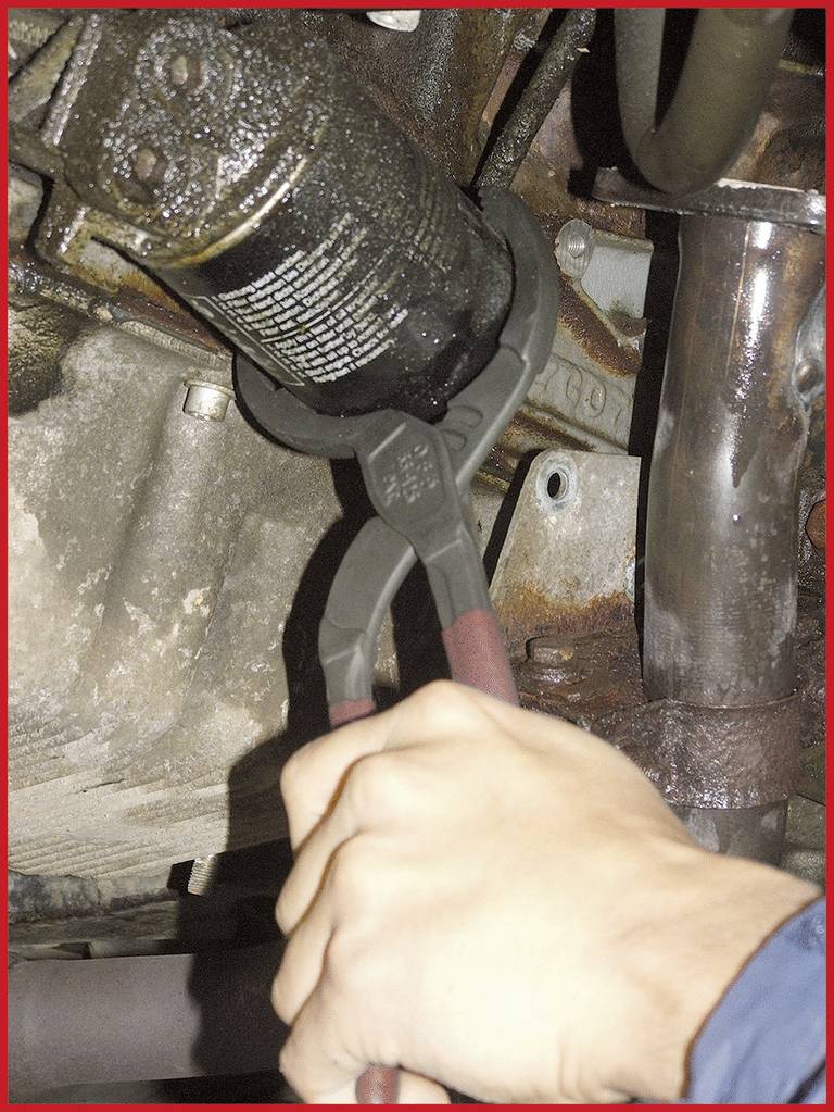 'Eine Person verwendet eine Rohrzange, um einen ölverschmierten Auto-Ölfilter in einem Motorraum zu entfernen.'