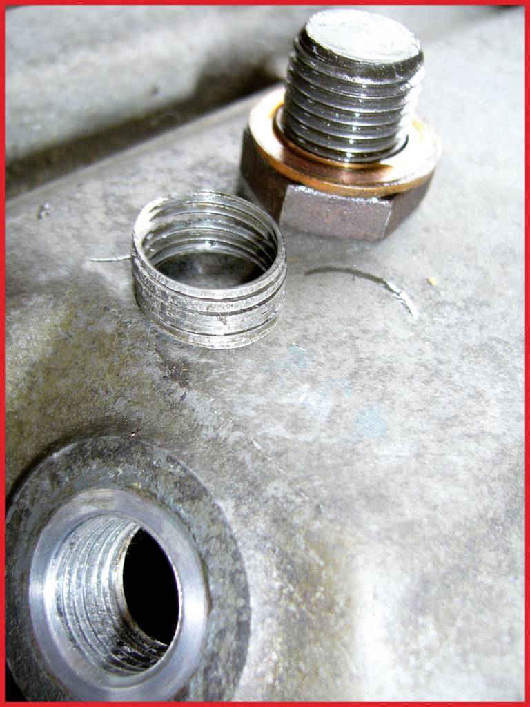 Eine beschädigte Gewindebohrung in einem Metallstück, neben einer Schraube mit einer Spiralfeder, die eine Gewindereparatur darstellt.