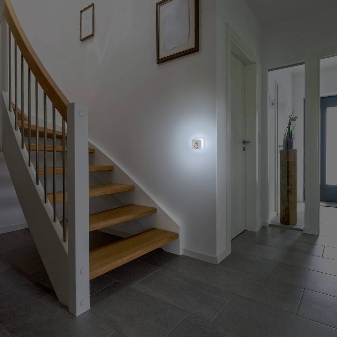 Eingangsbereich eines Hauses mit Treppe und Flur, moderne Dekoration und Wandleuchte, die ein sanftes Licht ausstrahlt.