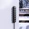 Eine schwarze Steckdosenleiste mit sechs Steckplätzen an einer Wand, im Hintergrund Schneelandschaft und holzfarbener Zaun.