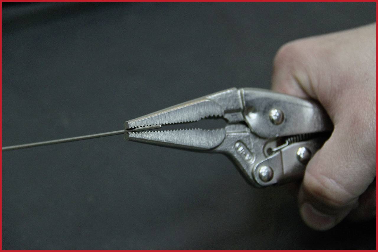 Eine Hand hält eine Zange, die ein dünnes Metalldrahtstück greift.