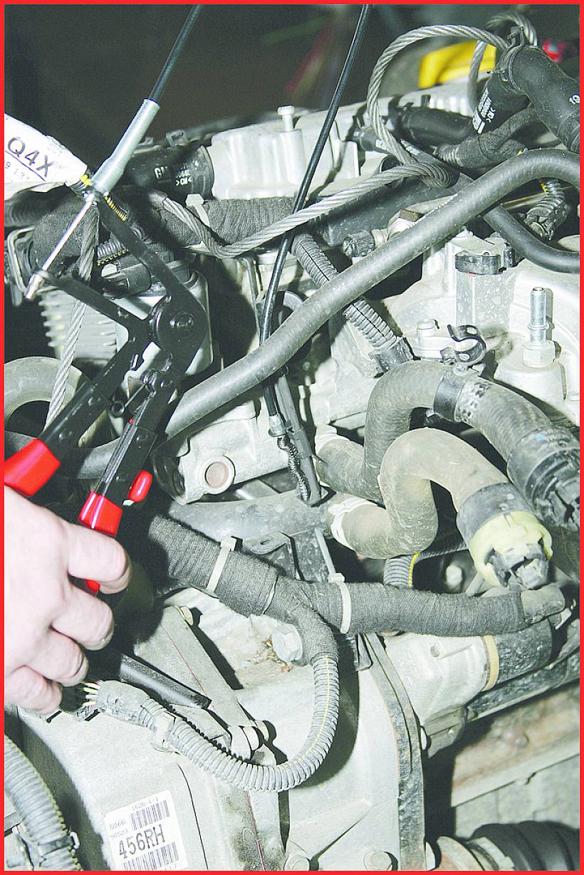 'Eine Person verwendet eine Zange, um Kabel an einem Automotor zu reparieren. Verschiedene Schläuche und Drähte sind sichtbar.'