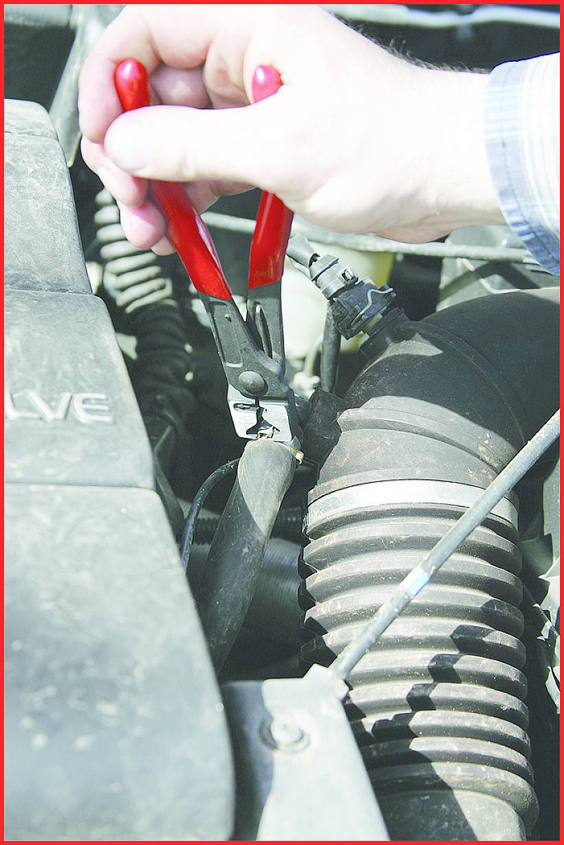 Eine Hand hält rote Zangen und repariert einen Teil des Motors, umgeben von Schläuchen und Motorabdeckungen, im Sonnenlicht.