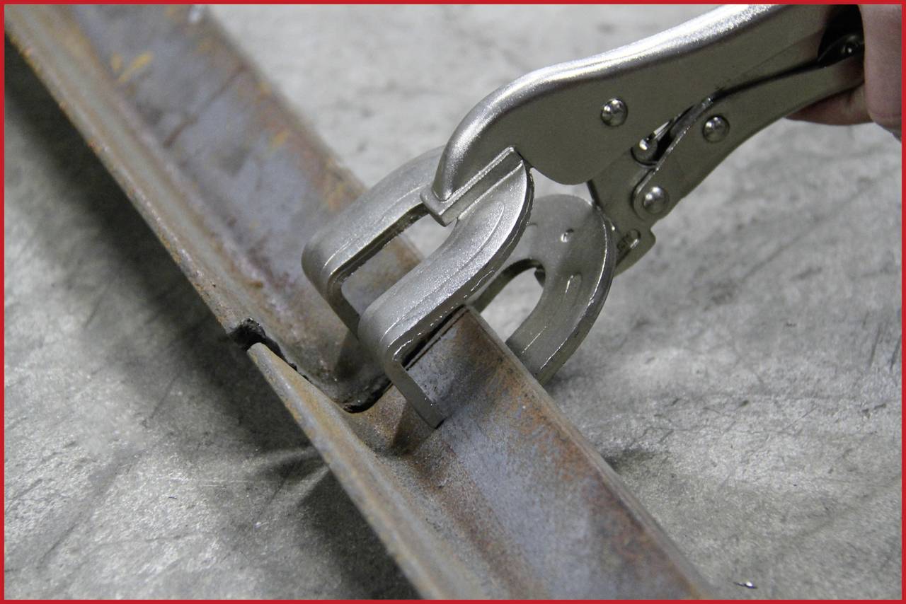 Ein Metallstück wird mit einer Handzange gebogen. Die Zange hält das Metall fest und formt es zu einem Winkel. Im Hintergrund ist eine Betonfläche sichtbar.
