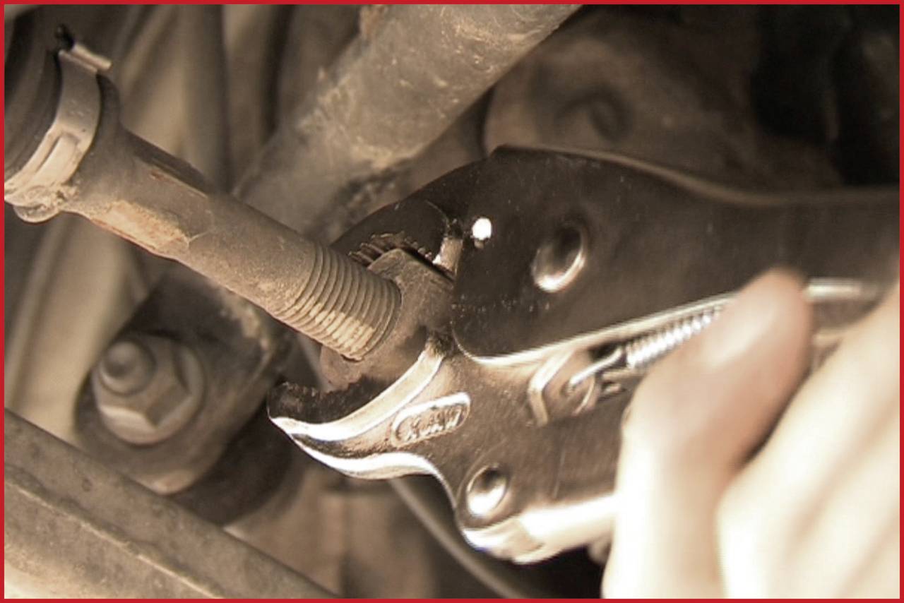Eine Hand hält eine Rohrzange und justiert einen Bolzen oder eine Schraube an einem Fahrzeugmotor.