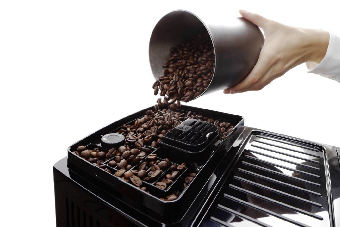 Eine Hand schüttet Kaffeebohnen aus einem Behälter in das Fach einer Kaffeemaschine.