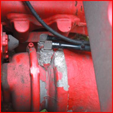 Rotes Industrieteil mit Kabeln und metallischem Verschleiß auf einer Oberfläche.