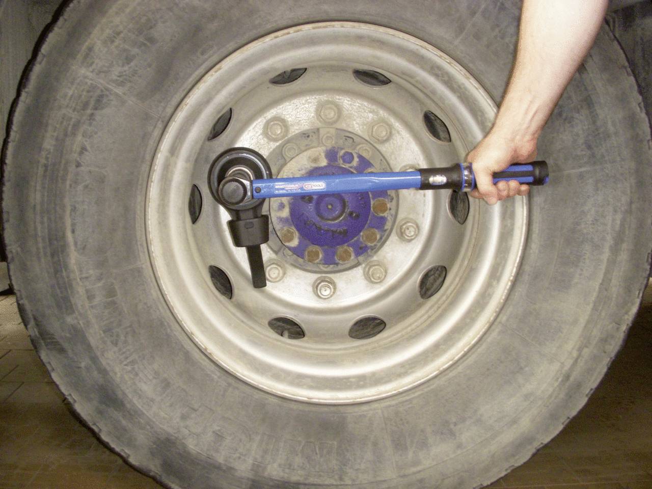 Ein Reifen wird mit einem Drehmomentschlüssel festgezogen. Eine Hand hält den Schlüssel am Rad eines großen Fahrzeugs.