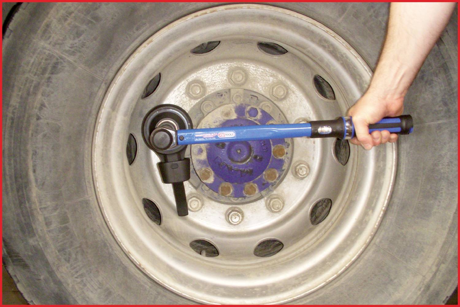 Ein großer Lkw-Reifen wird mit einem Drehmomentschlüssel festgezogen. Eine Hand hält das Werkzeug am Rad.