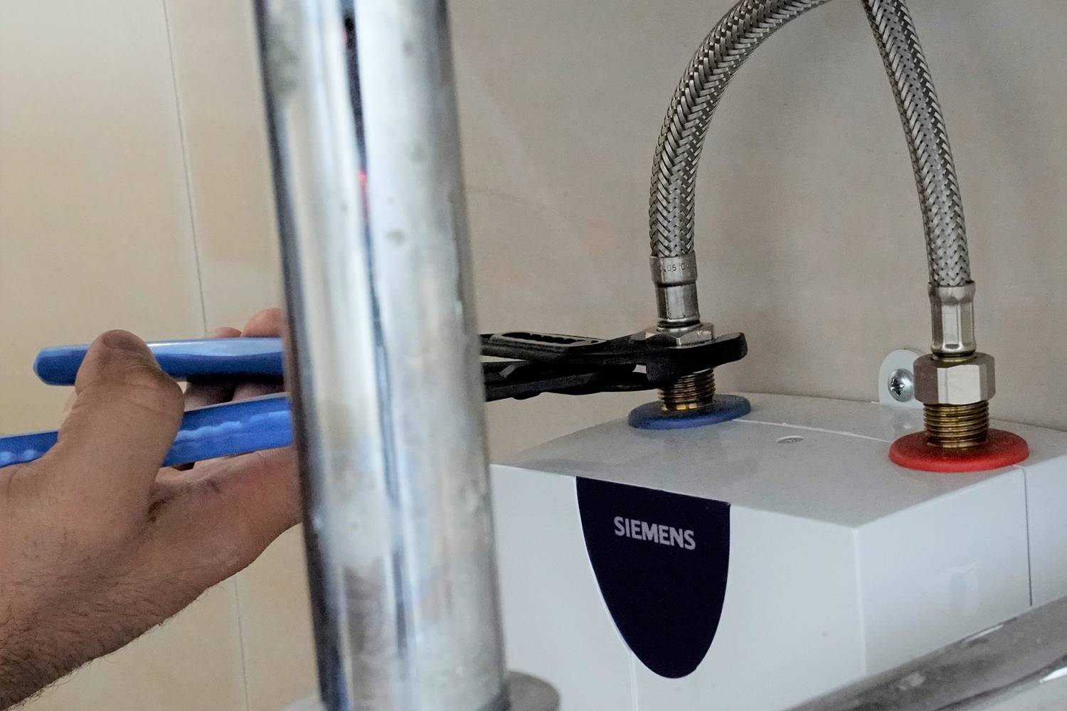 Eine Person repariert eine Wasserleitung unter einem Waschbecken, verwendet eine Zange, um eine Armatur an einem Geräteanschluss zu festigen.