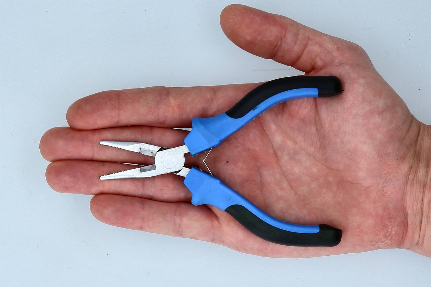 Eine Hand hält eine kleine Zange mit blauen Griffen, die für feinmechanische Arbeiten nützlich ist.