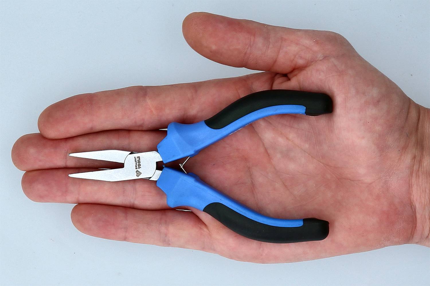 Eine Hand hält eine kleine Zange mit blauen Griffen. Die Zange ist geöffnet und liegt in der Handfläche auf, um ihre Größe zu zeigen.