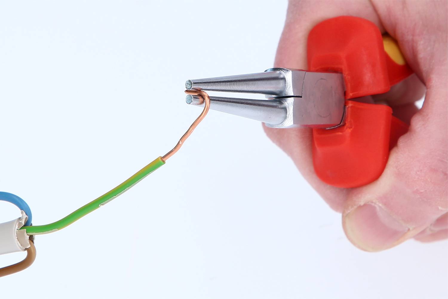 Eine Hand hält eine rote Zange, die einen Kupferdraht biegt. Der Draht ist teils isoliert und teils unverhüllt, es wird daran gearbeitet.