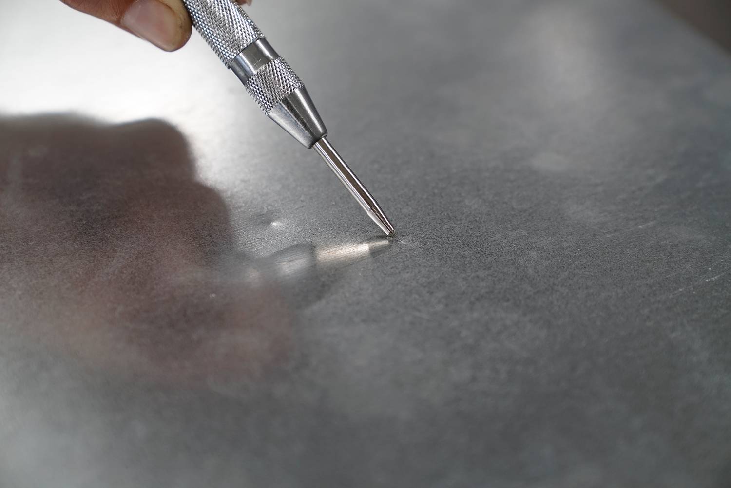 'Person hält einen Metallstift auf eine glatte Metalloberfläche, um eine Markierung anzubringen.'