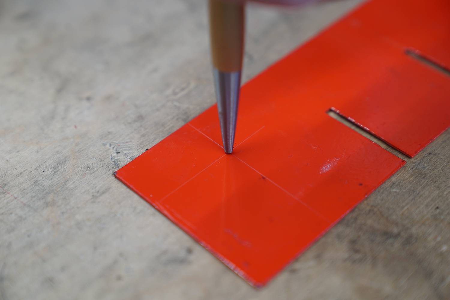 Eine Person markiert mit einem silbernen Stift präzise Punkte auf einer roten Schablone, die auf einem Tisch liegt.