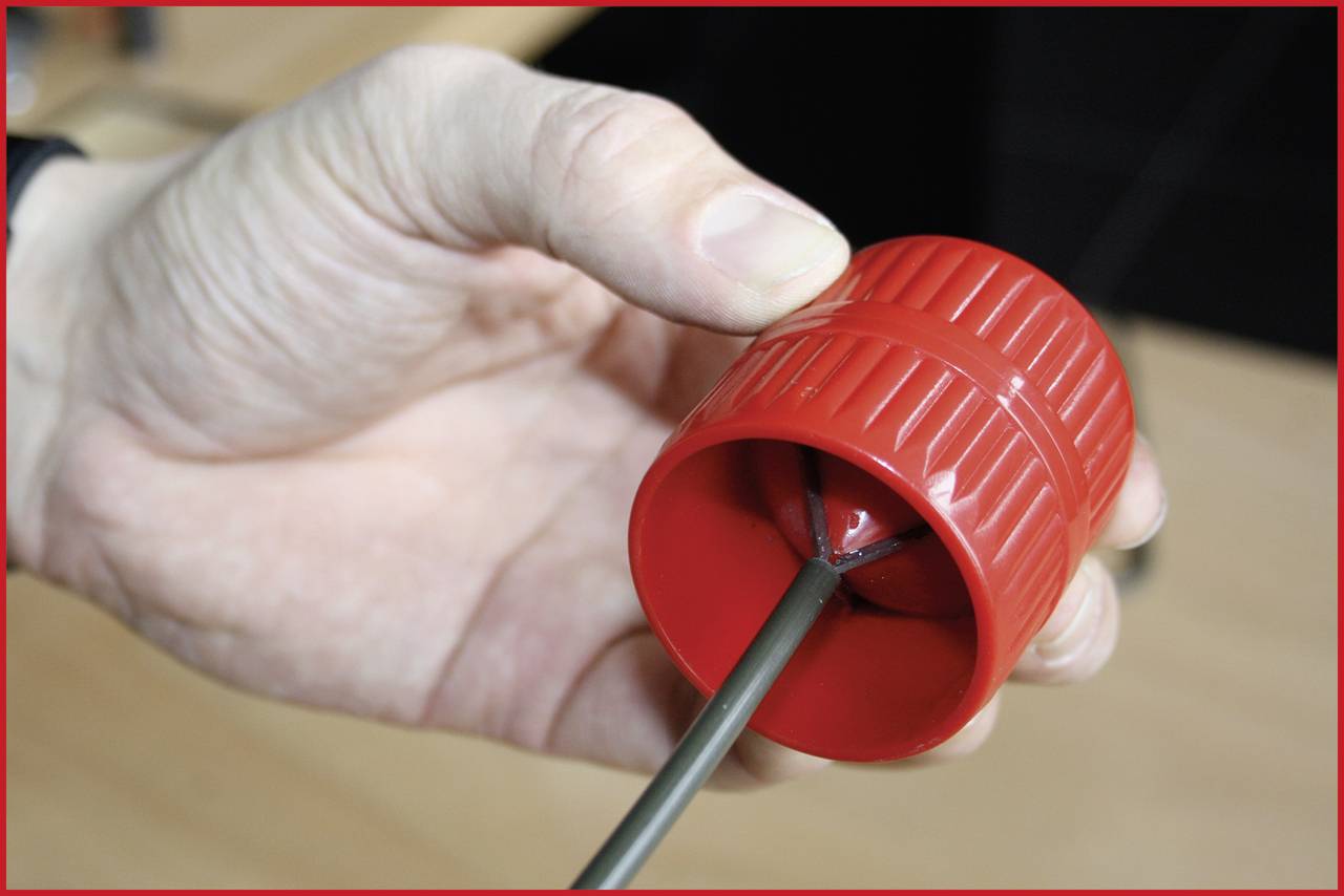 Eine Hand hält einen roten Spitzer, der auf einen Stift aufgesteckt wird. Der Spitzer ist zylinderförmig und geriffelt.