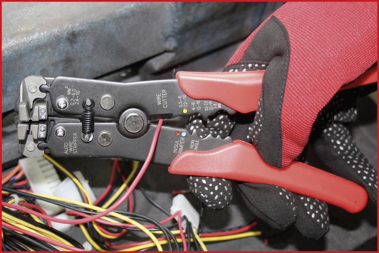 Person hält einen Drahtschneider mit roten Griffen und schneidet rote und gelbe Kabel in einer Elektrikerkontextumgebung.