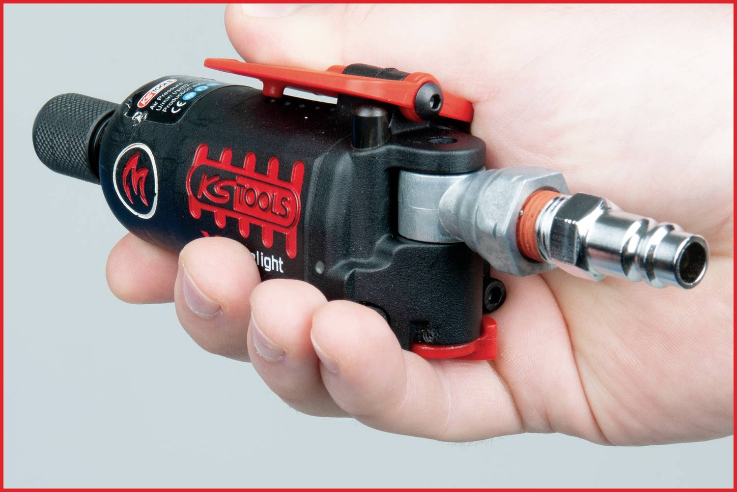 Eine Hand hält einen handlichen pneumatischen Winkelschleifer von KS Tools, schwarz mit roten Akzenten und einem Luftanschluss.