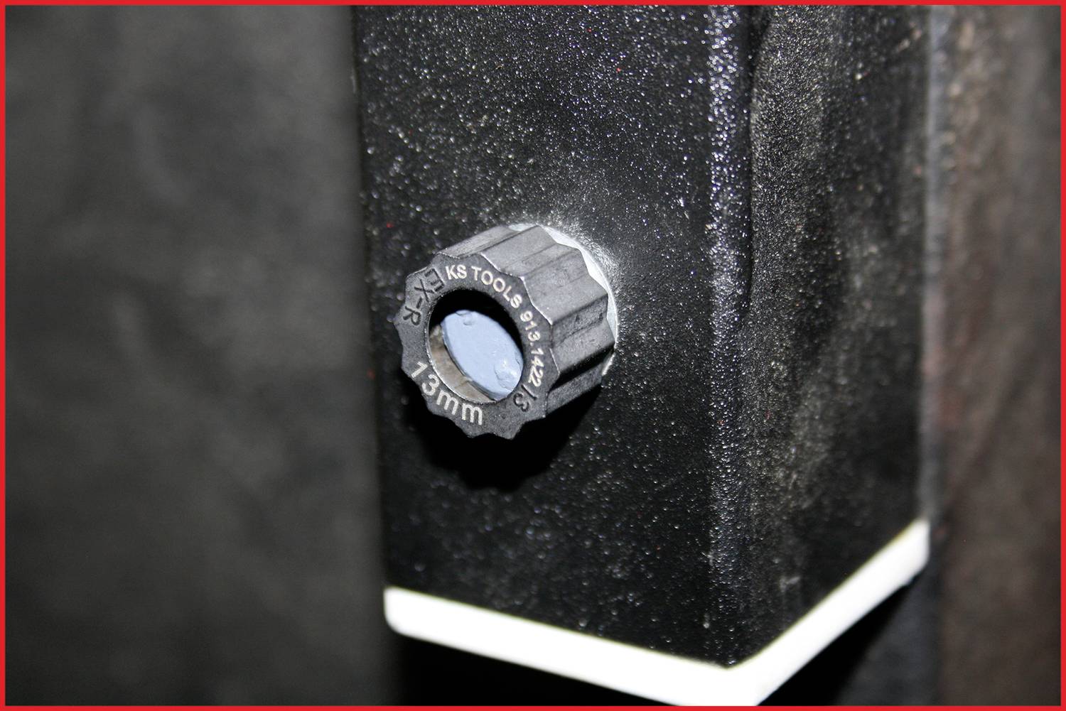 Schwarze Schraube mit Skala von '13mm' an einem Metallgehäuse, vermutlich Teil eines Werkzeugs oder einer Maschine.