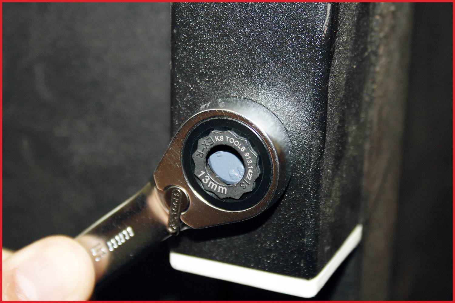 Nahaufnahme eines Ringschlüssels, der auf eine 13 mm Sechskantschraube angesetzt wird, möglicherweise an einem mechanischen Gerät angebracht.