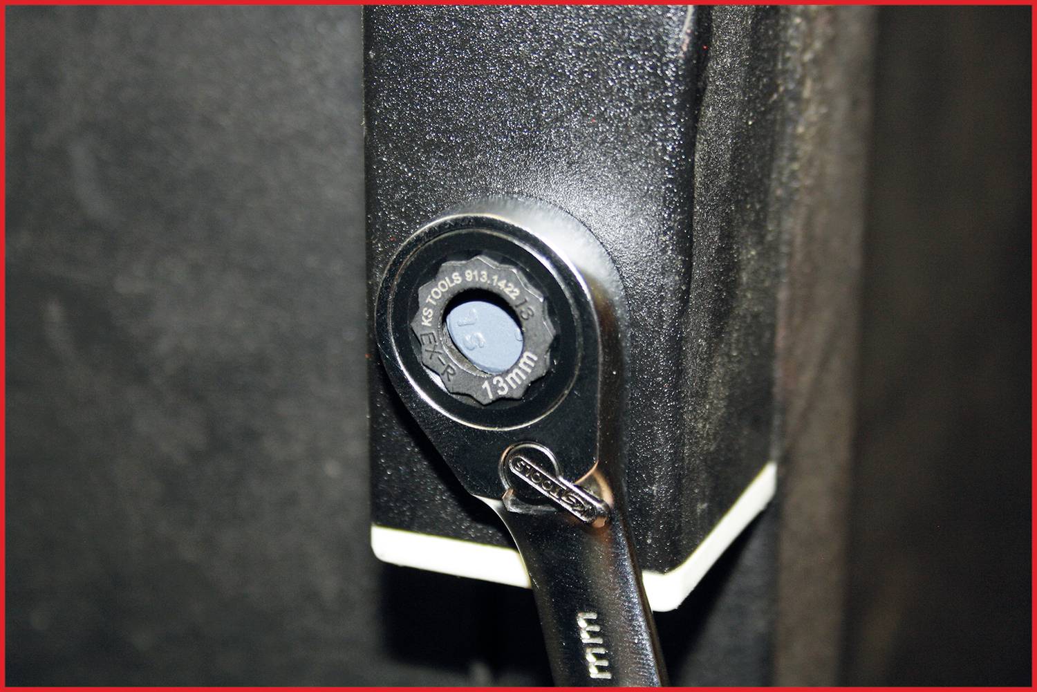 'Eine Ratsche befestigt an einer Schraube an einem schwarzen Metallstück. Der Schraubenkopf ist mit der Größe 13 mm markiert.'