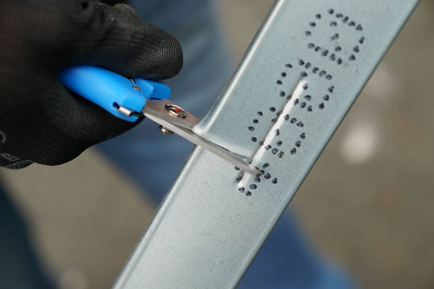 Person schneidet mit einer blauen Zange Löcher in ein Metallprofil. Die Aktion deutet auf eine handwerkliche Tätigkeit hin.