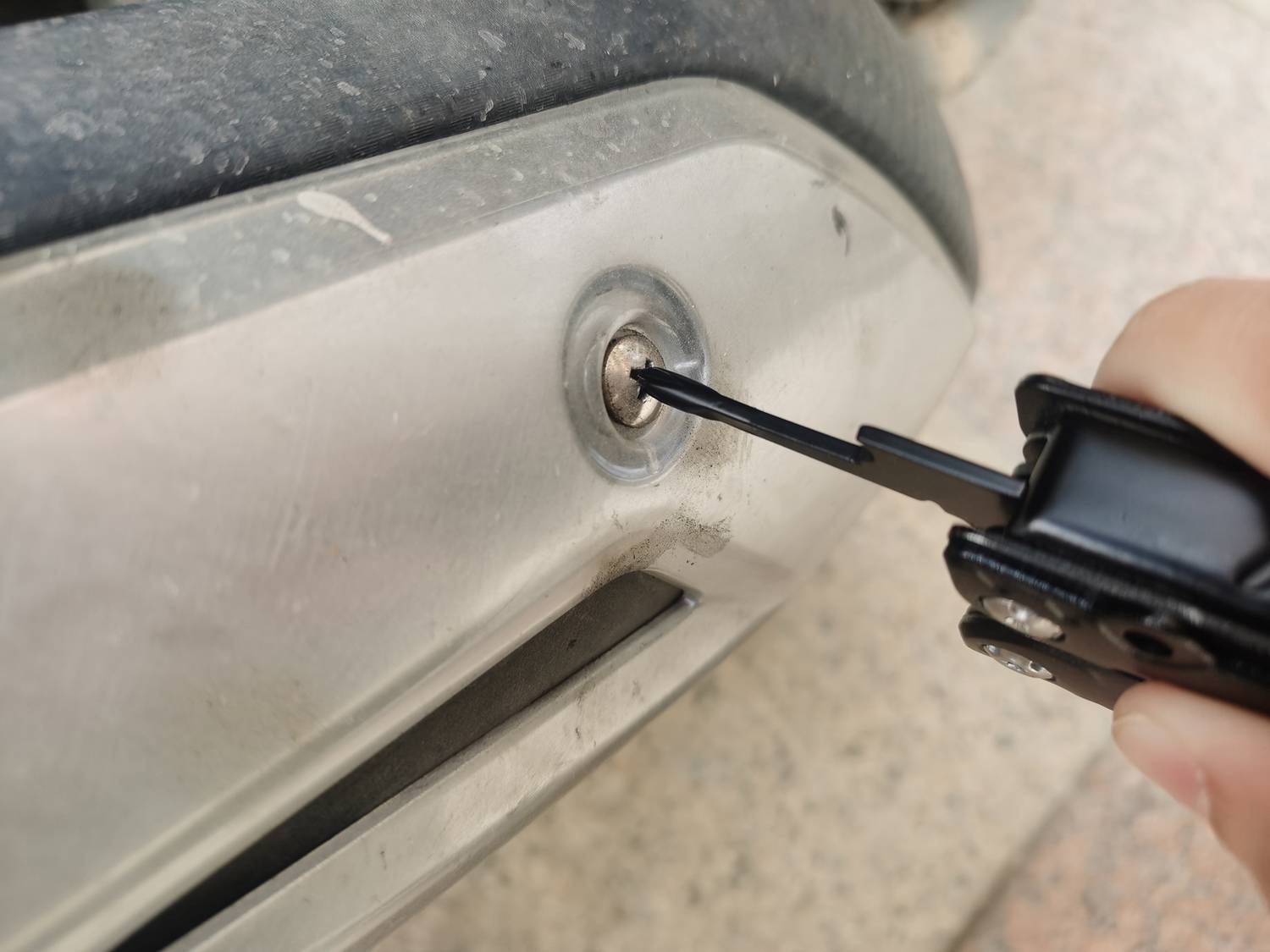 'Eine Person schraubt mit einem schwarzen Werkzeug eine Schraube an einem metallischen Objekt fest.'