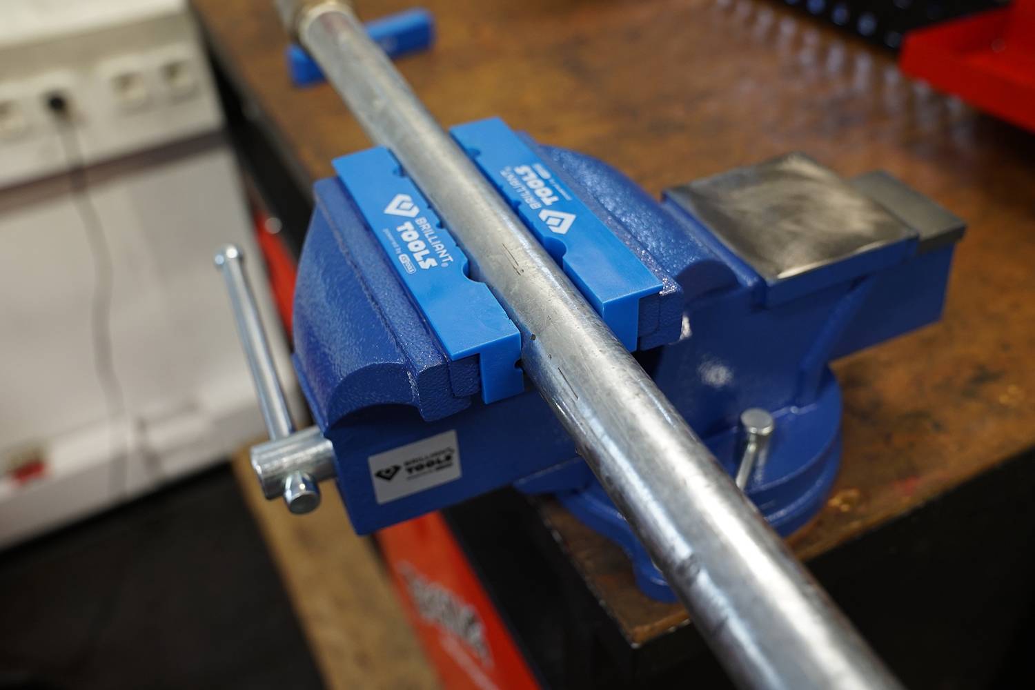 Eine Metallstange ist in einem blauen Schraubstock auf einem Werkbanktisch eingespannt.