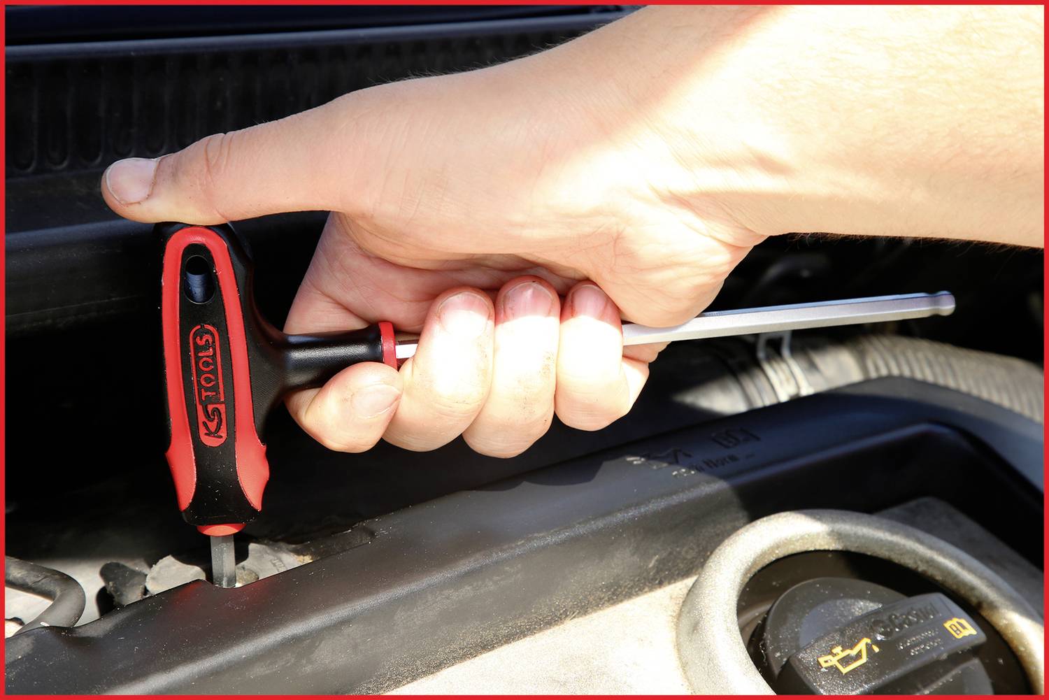 Eine Hand hält einen Schraubendreher und zieht eine Schraube im Motorraum eines Autos an.