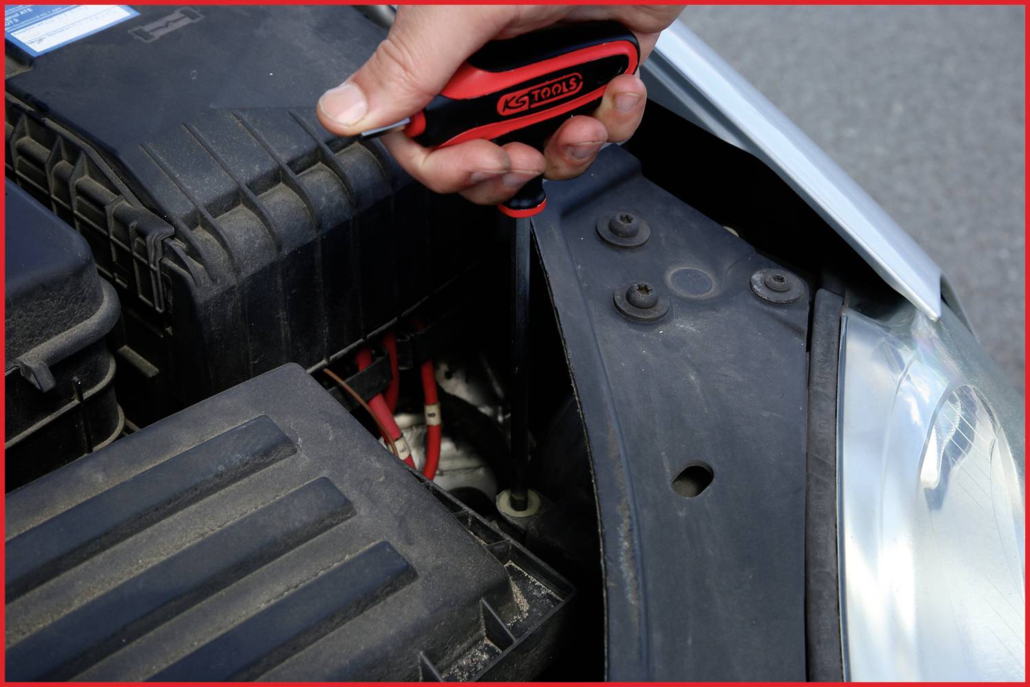 Eine Person repariert den Motor eines Autos mit einem Schraubendreher. Im Fokus sind der Motorraum und der Schraubendreher in der Hand.