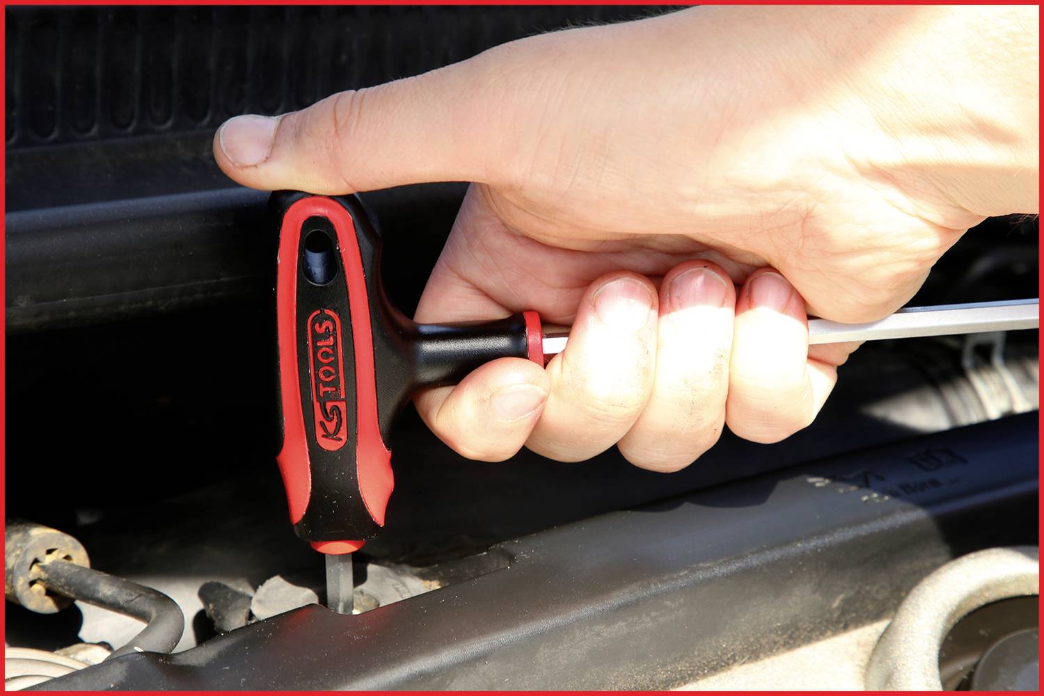 Eine Hand hält einen Schraubendreher und zieht eine Schraube im Motorraum eines Fahrzeugs fest.