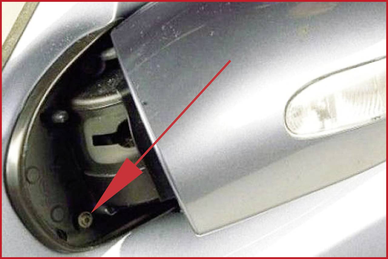 Ein Pfeil zeigt auf eine Schraube hinter der demontierten Stoßstange eines Autos.