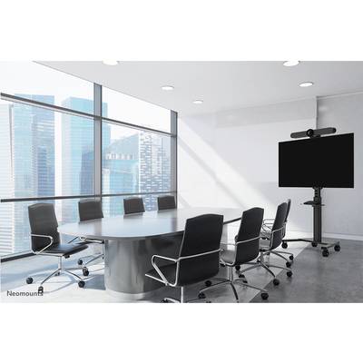 Konferenzraum mit großem ovalen Tisch, acht schwarzen Stühlen und großem Bildschirm auf einem Ständer; Fenster mit Stadtblick im Hintergrund.