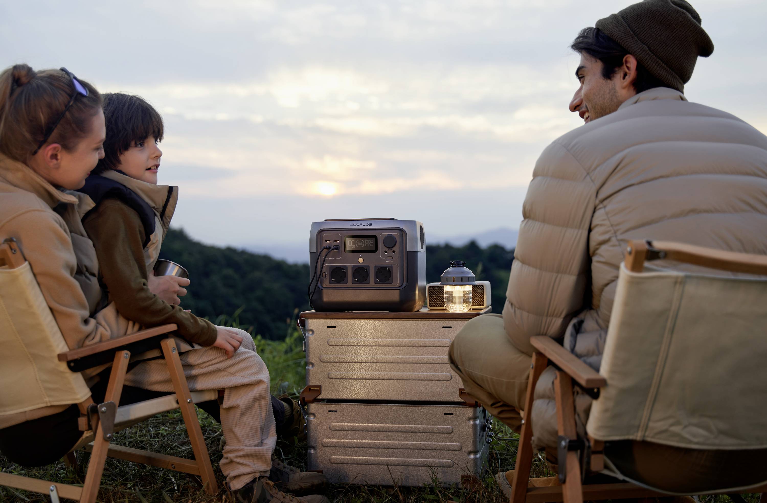 Personen sitzen draußen im Sonnenuntergang, kringeln sich um eine tragbare Energiequelle. Stimmung ist entspannt und gemütlich.