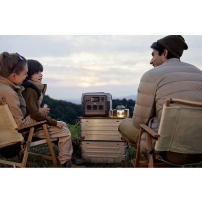 Personen sitzen draußen im Sonnenuntergang, kringeln sich um eine tragbare Energiequelle. Stimmung ist entspannt und gemütlich.