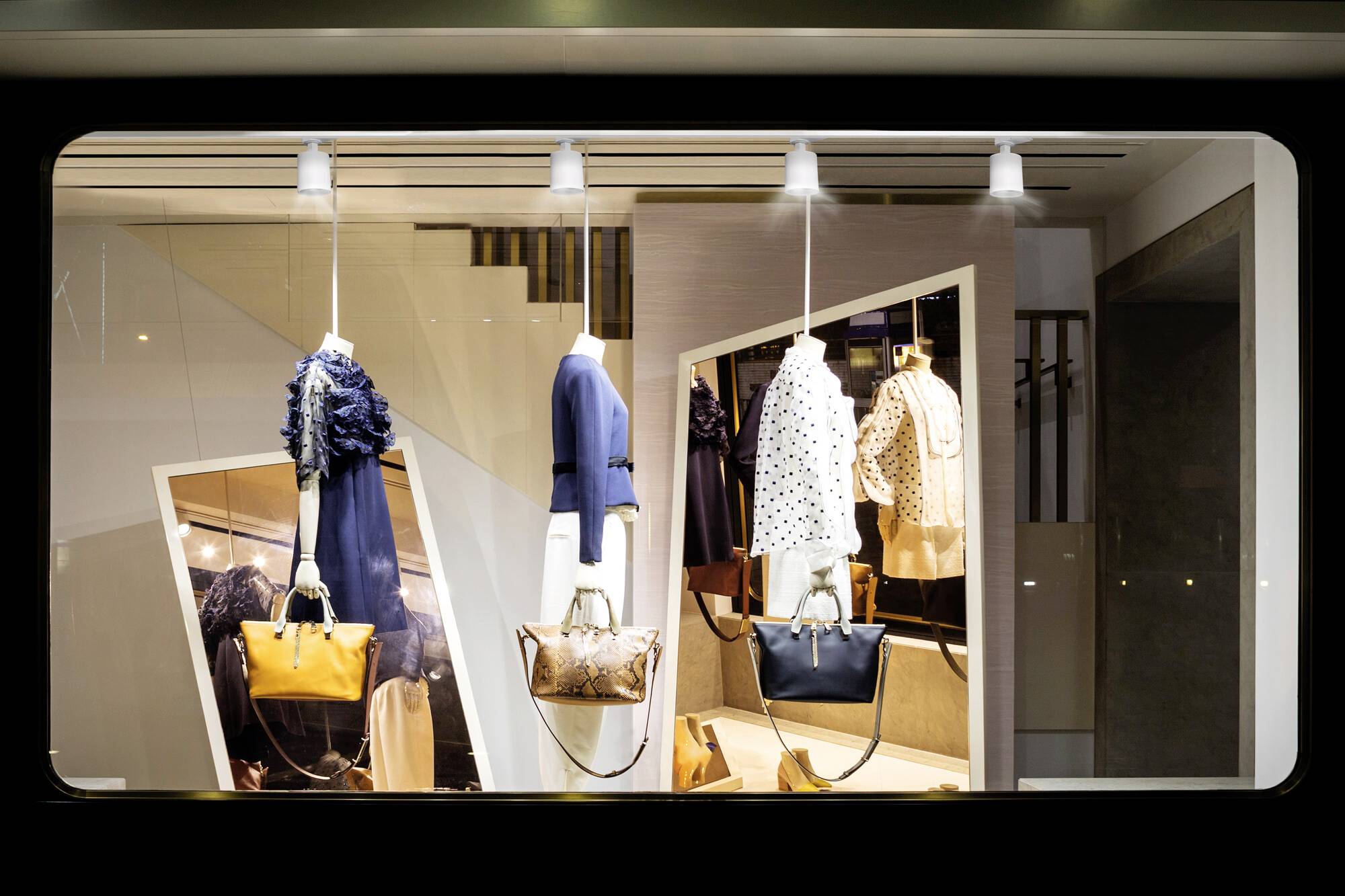 Schaufenster mit eleganter Kleidung: drei Outfits auf Puppen, je eins in Blau, Weiß mit Punkten und Gold, mit passenden Handtaschen.