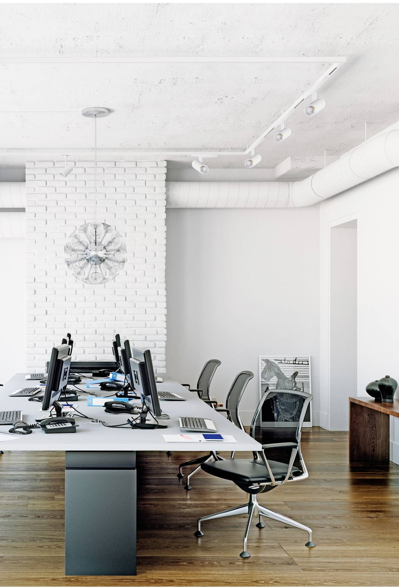 Ein moderner, weißer Büroraum mit Reihen von Schreibtischen und Computern, leeren schwarzen Stühlen, Holzboden, weißer Backsteinwand.