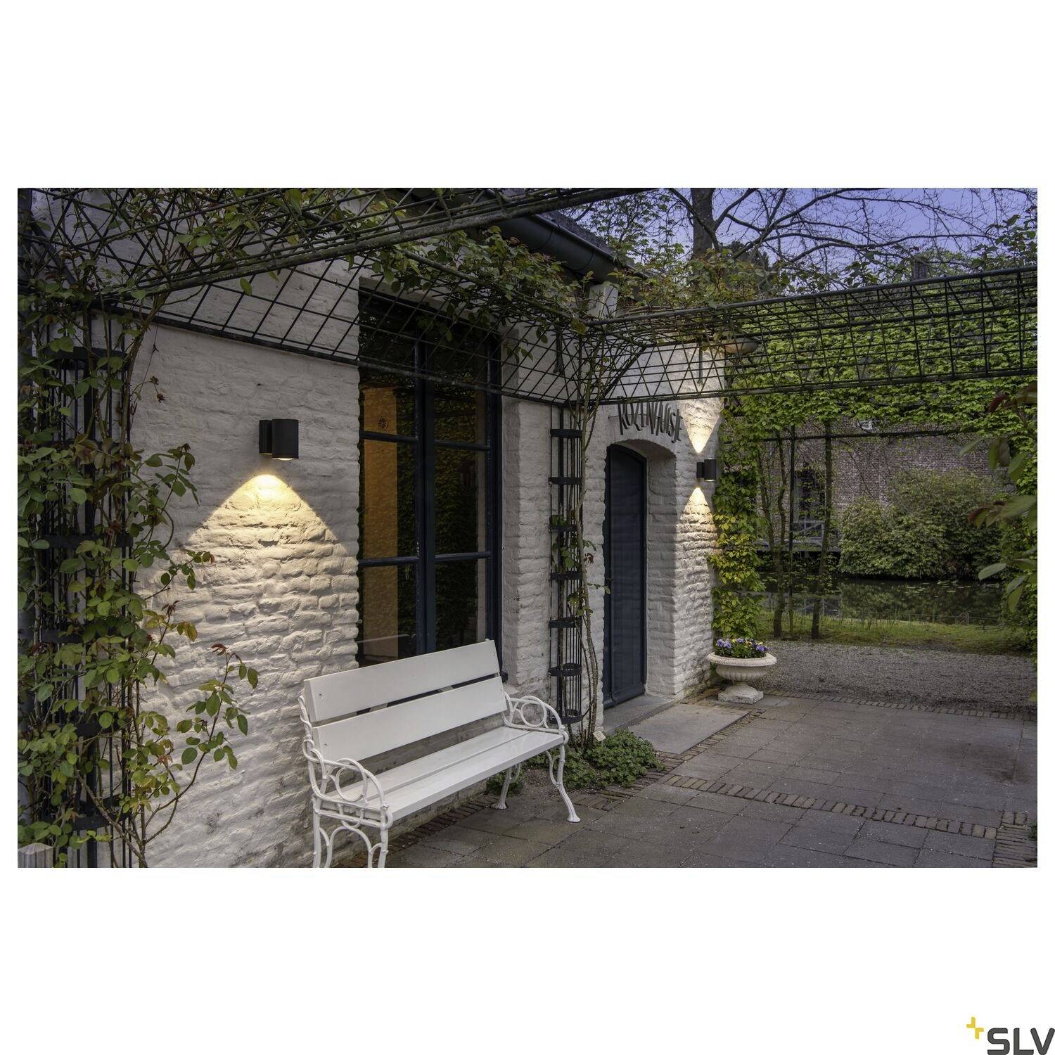 Außenbereich eines Hauses mit Steinmauer, Bank und Laternen, die sanft beleuchtet sind, um eine einladende Atmosphäre zu schaffen.