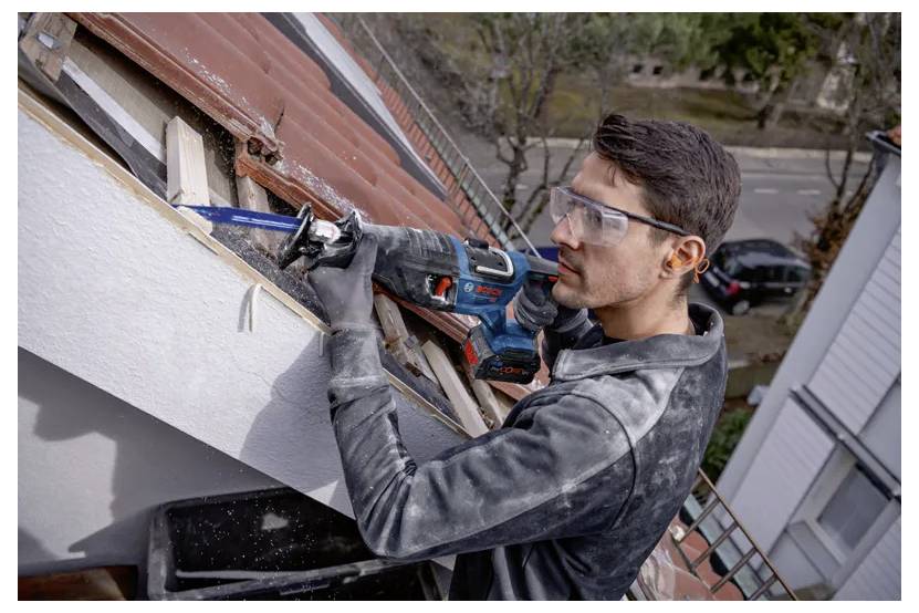 Eine Person mit Sicherheitsbrille verwendet eine Kreissäge, um Holz auf einem Dach zu schneiden und dabei Fokus und Konzentration bei einer Heimwerker-Renovierungsaufgabe zu zeigen.