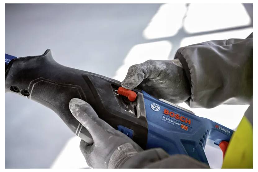 Person, die ein Bosch-Werkzeug verwendet, Handschuhe und einen Schutzmantel trägt und die Einstellungen am Griff des Werkzeugs in einer Werkstatt anpasst.