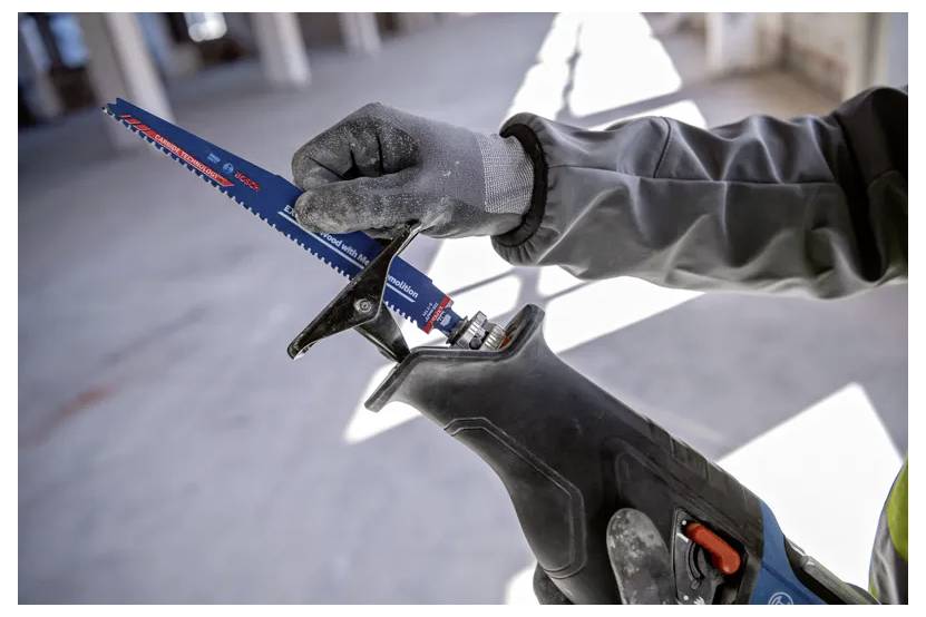 Eine Person mit Handschuhen verwendet eine Säbelsäge und wechselt das Sägeblatt in einer Baukonstruktionsumgebung.