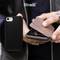 Eine Person hält ein Smartphone mit einer schwarzen Schutzhülle und einem kleinen dunkelbraunen Klappetui in der Hand.
