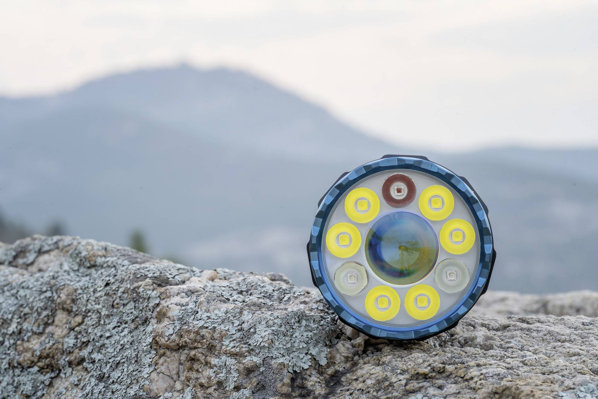 Taschenlampe mit mehreren LED-Lampen liegt auf einem Felsen, im Hintergrund sind unscharfe Berge zu sehen.